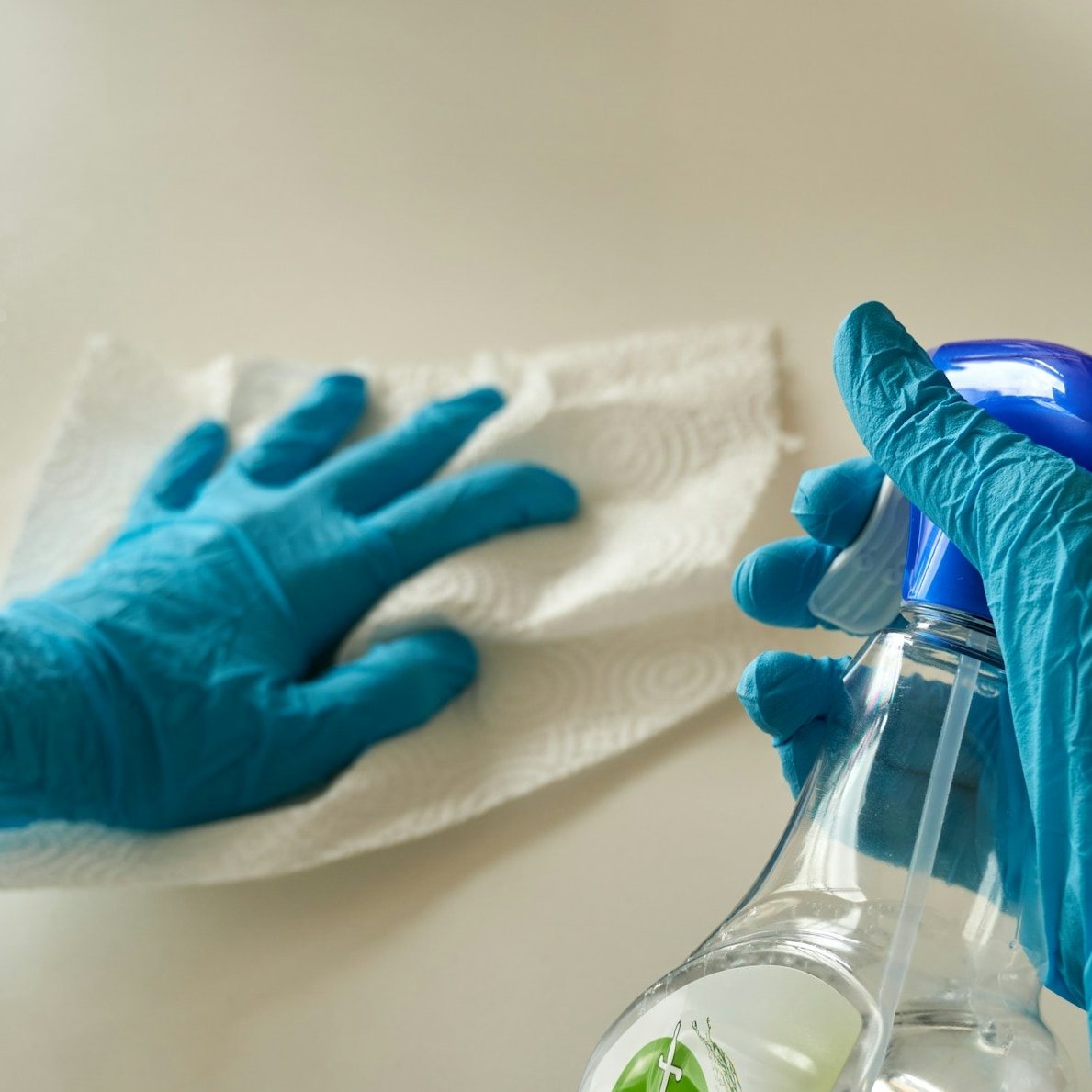 Gloved hands spraying cleaner and wiping a counter with a paper towel