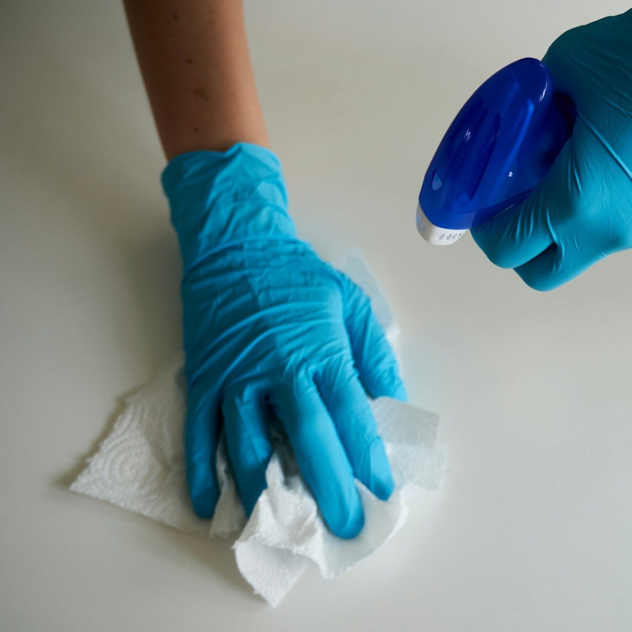Gloved hands wiping a clinical surface with disinfectant and a paper towel
