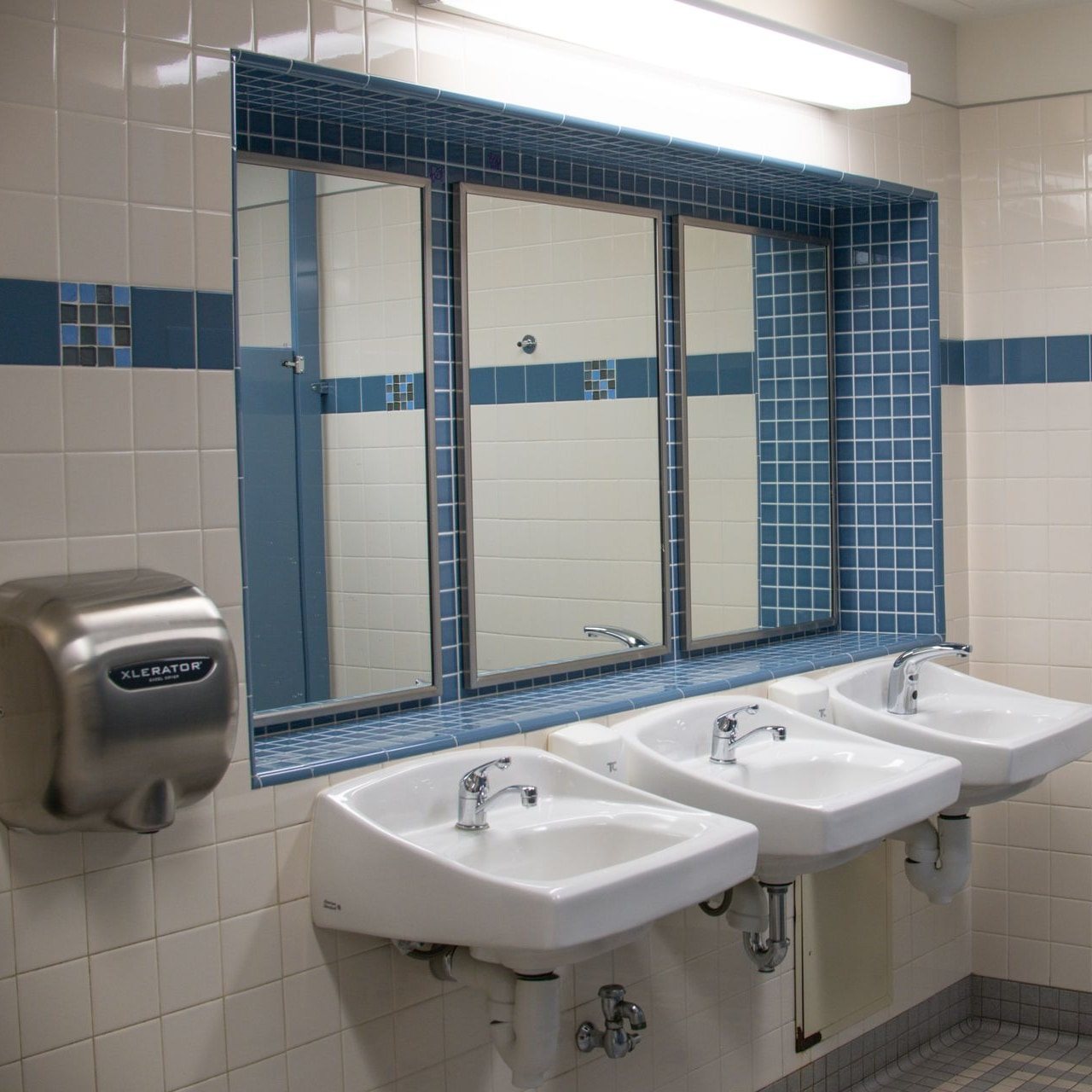 Tiled public restroom with three sinks and a wall-mounted hand dryer
