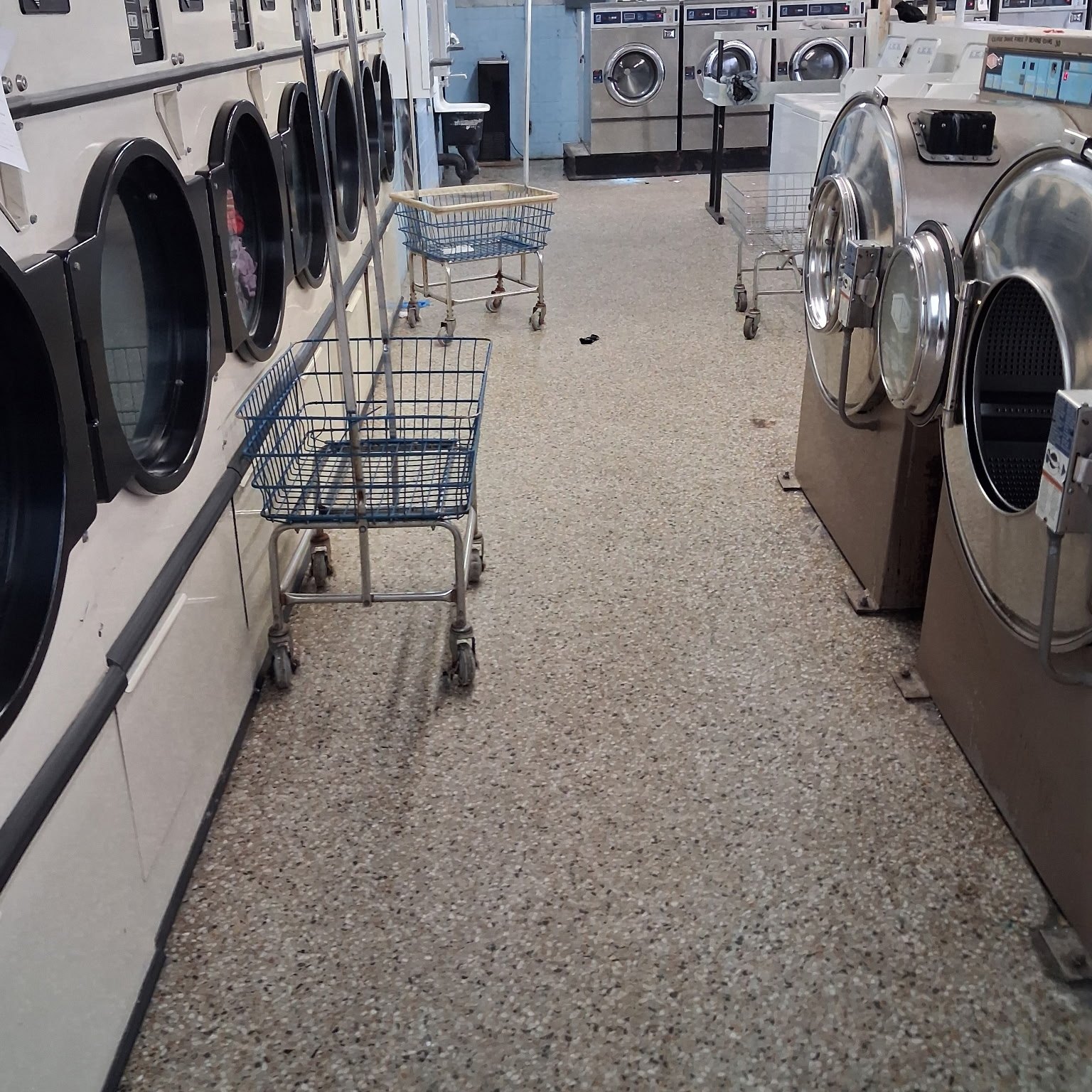 The same laundry room before cleaning, with carts left in the aisle and a marked floor
