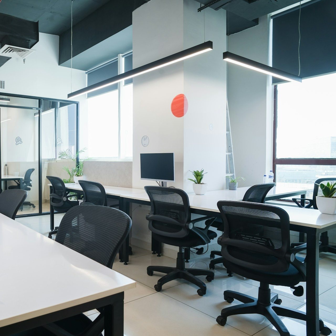 Bright coworking floor with white desks, glass meeting room and potted plants