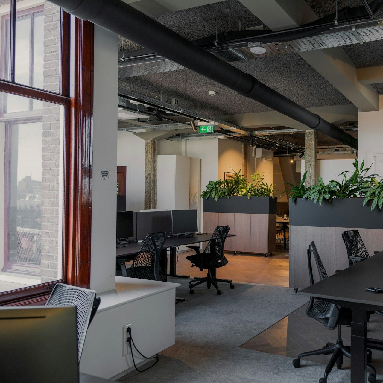 Open-plan loft office with exposed ductwork, planter dividers and desk rows